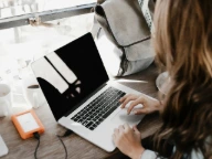 girl wearing grey long-sleeved shirt using MacBook Pro on brown wooden table
